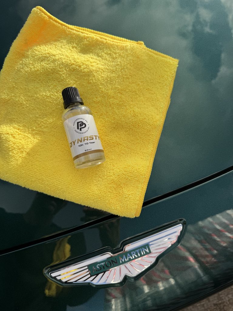 Bottle of ceramic coating solution on a yellow cloth, placed on green Aston Martin car
